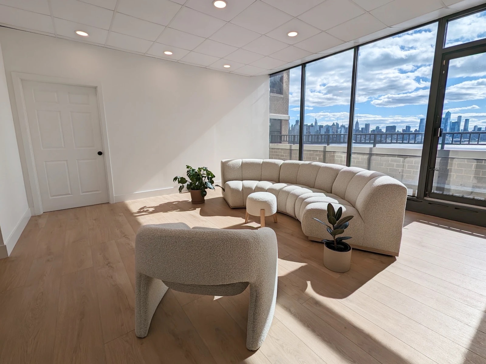 Sunlit studio lounge at HudsonDesk with a curved bouclé sofa facing floor-to-ceiling skyline windows